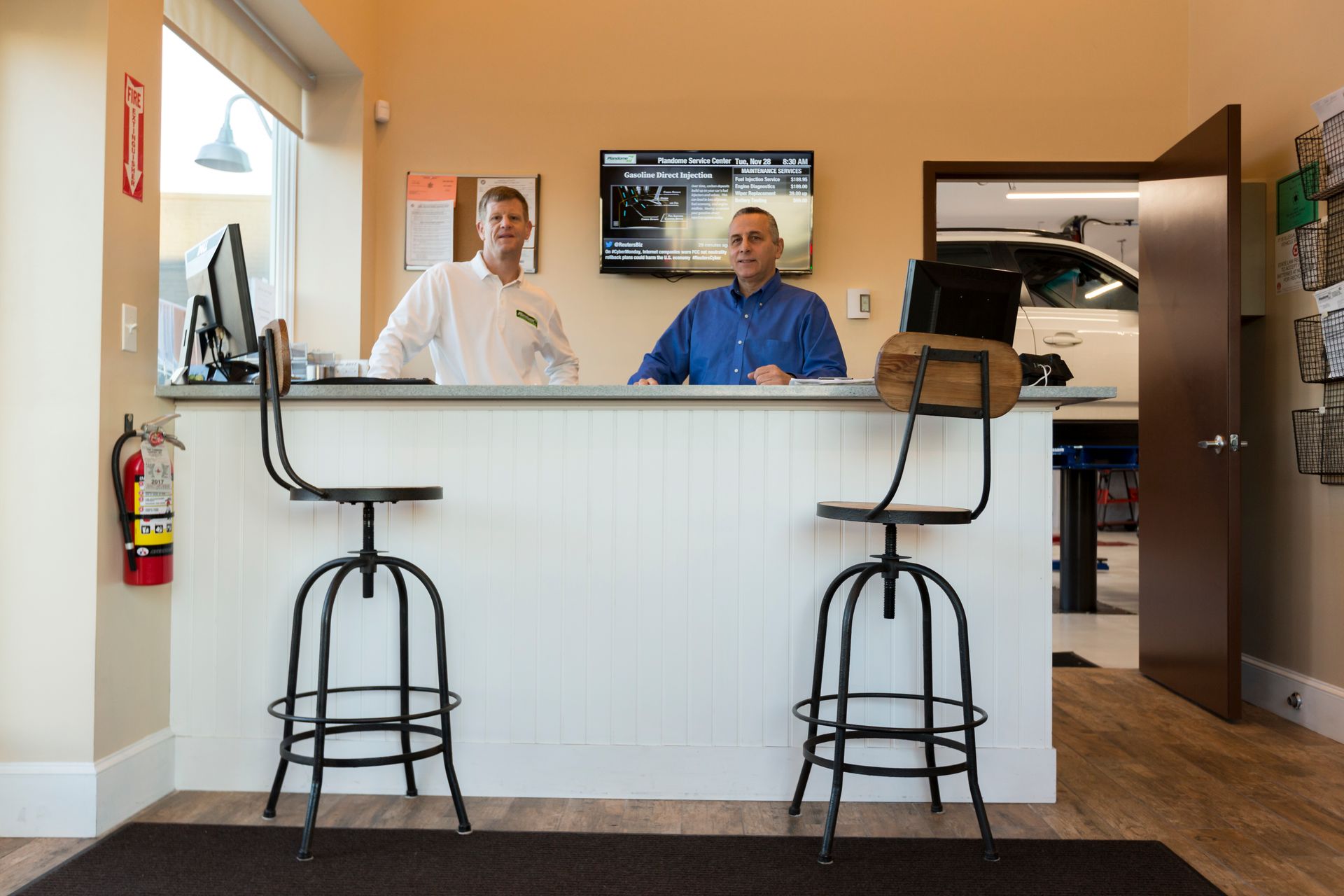 Two men at a white counter in an auto shop, one in a blue shirt, the other in a white shirt. | Plandome Service Center