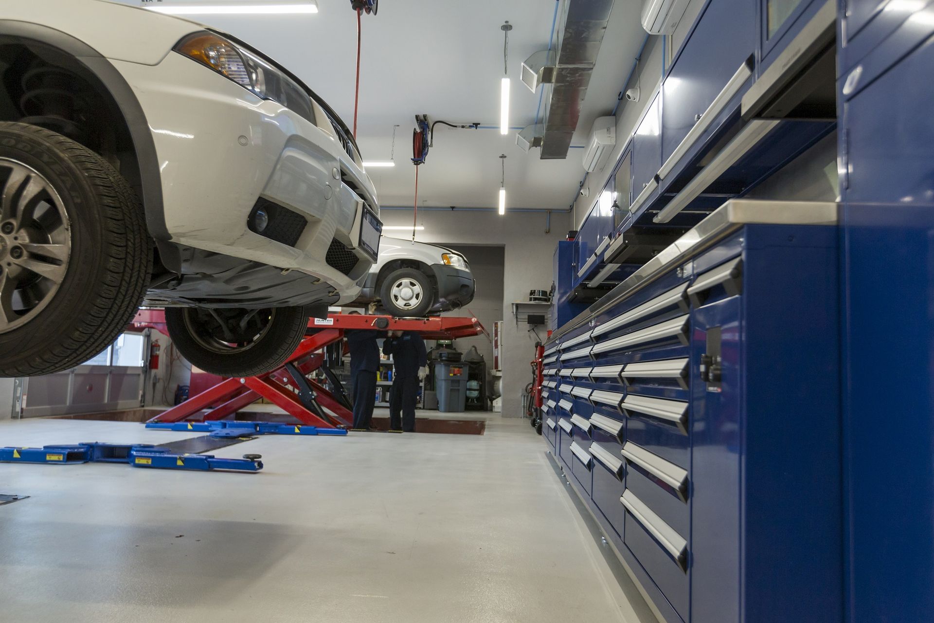 White car on a lift in a blue-walled auto shop with tool cabinets. | Plandome Service Center