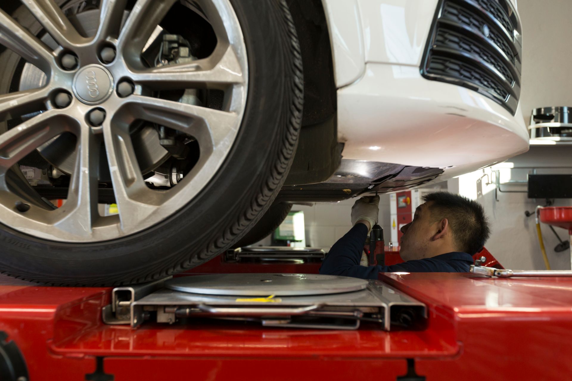 Mechanic working under a white car on a lift, examining the undercarriage. | Plandome Service Center