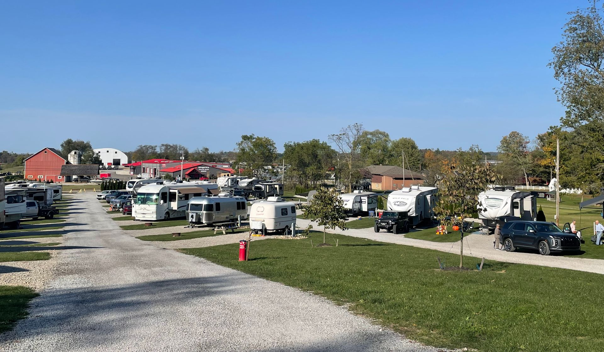 RV park with gravel driveways, green grass, and various RVs parked under a blue sky.