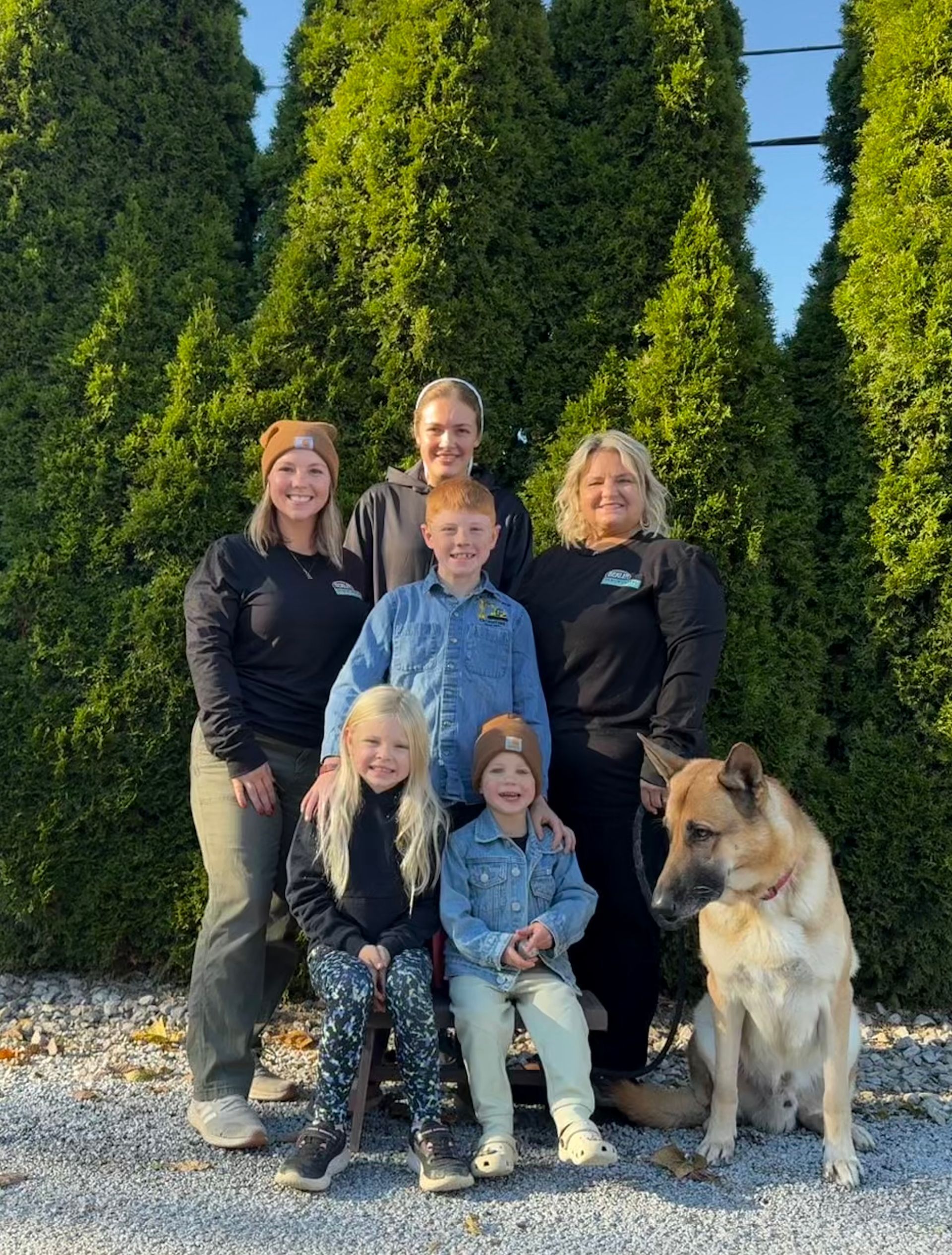 A group of people and a dog stand on a porch. Autumn leaves decorate the door.