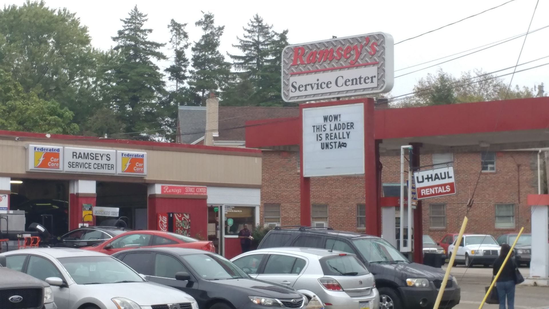 Ramsey's Service Center with cars in front. Red and white sign, a brick building, and a cloudy sky. | Ramsey's Service Center