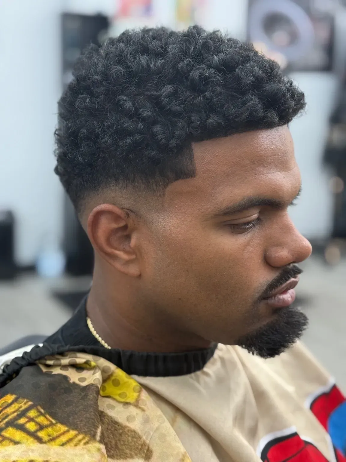 Man with curly dark hair and a faded haircut, wearing a barber's cape.