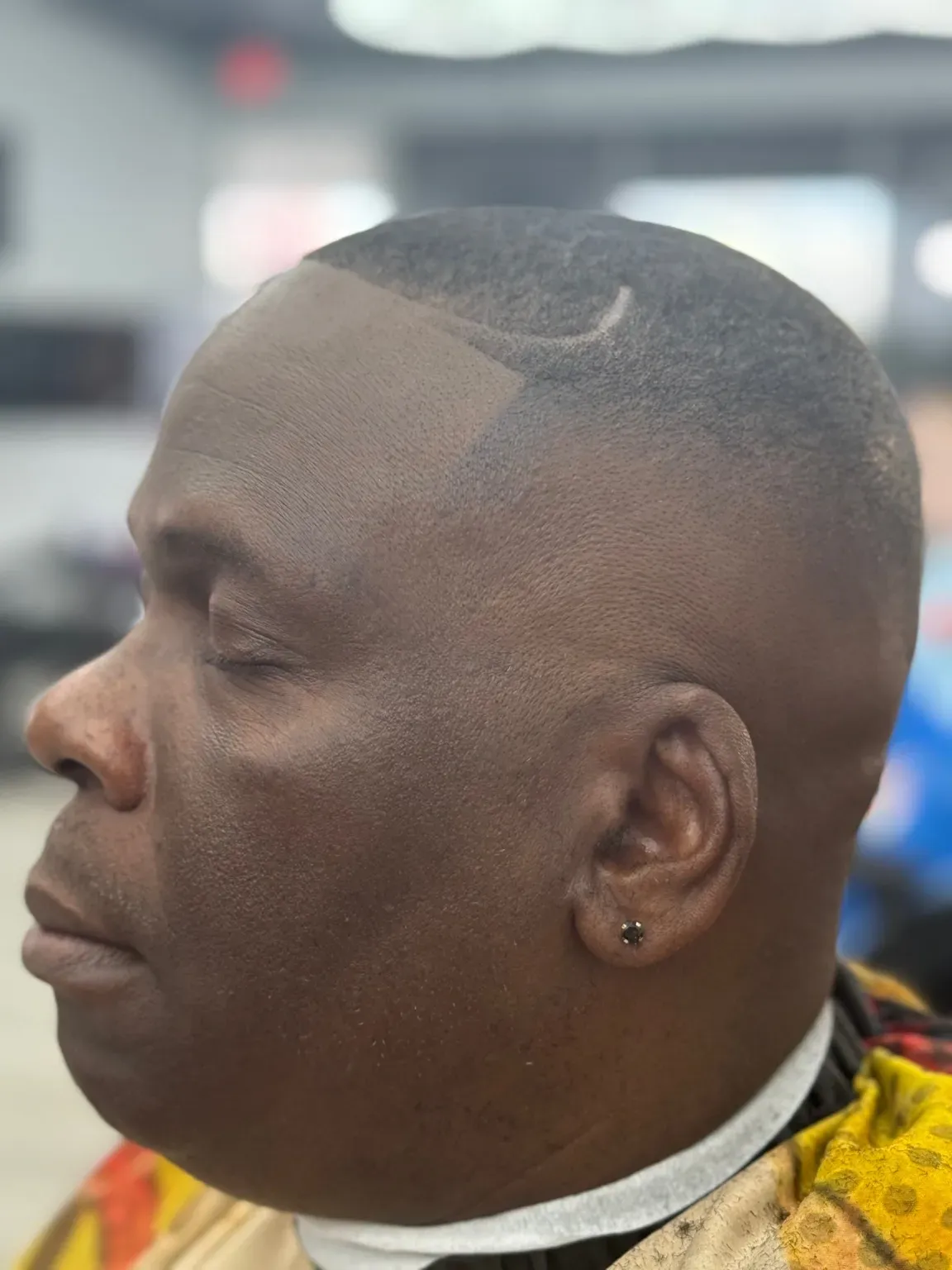 Man with a neatly-cut, faded haircut and design shaved into the hairline. Wearing a barber's cape.