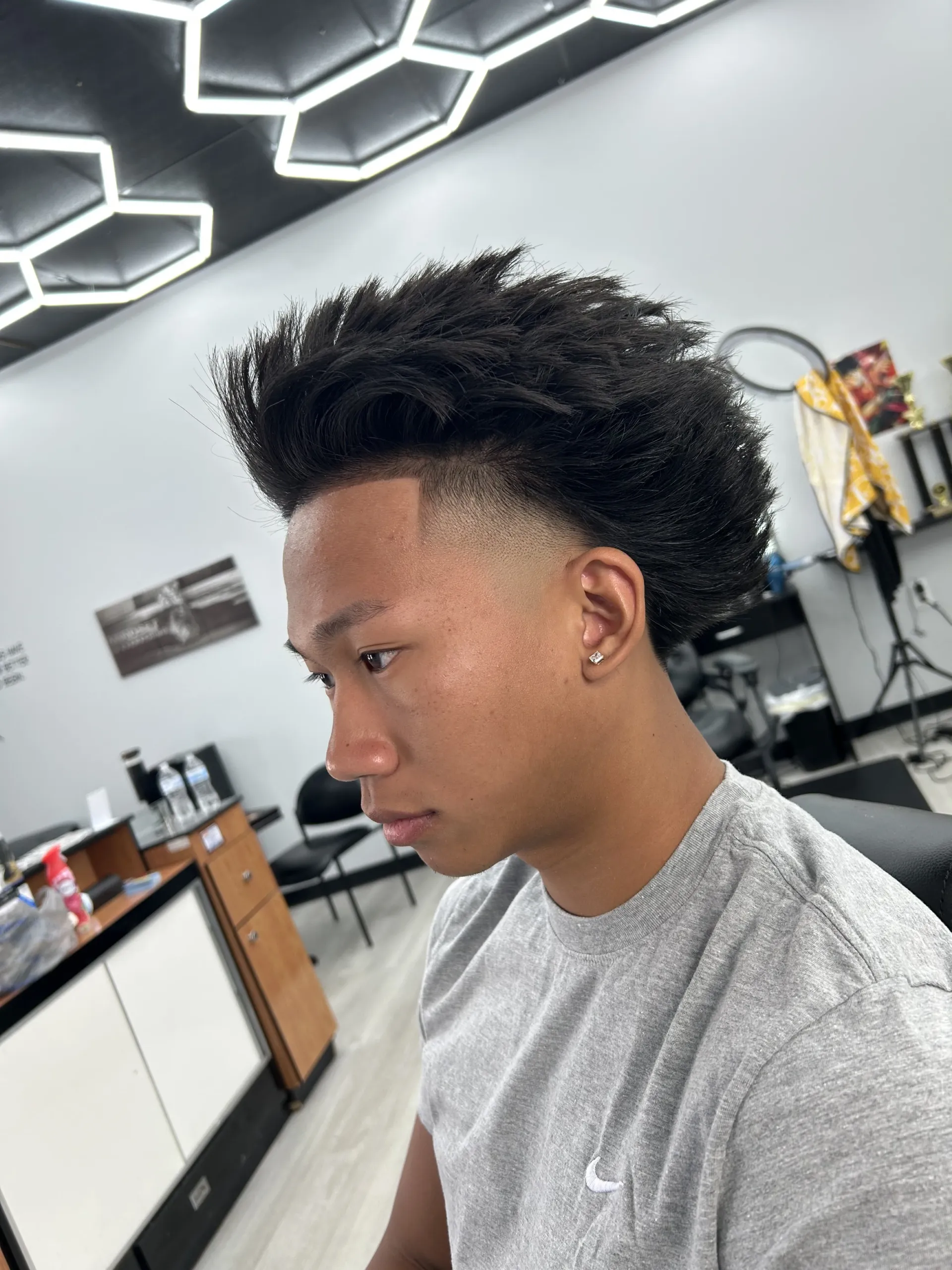 Man with a high-top fade haircut, side profile, in a brightly lit barbershop.