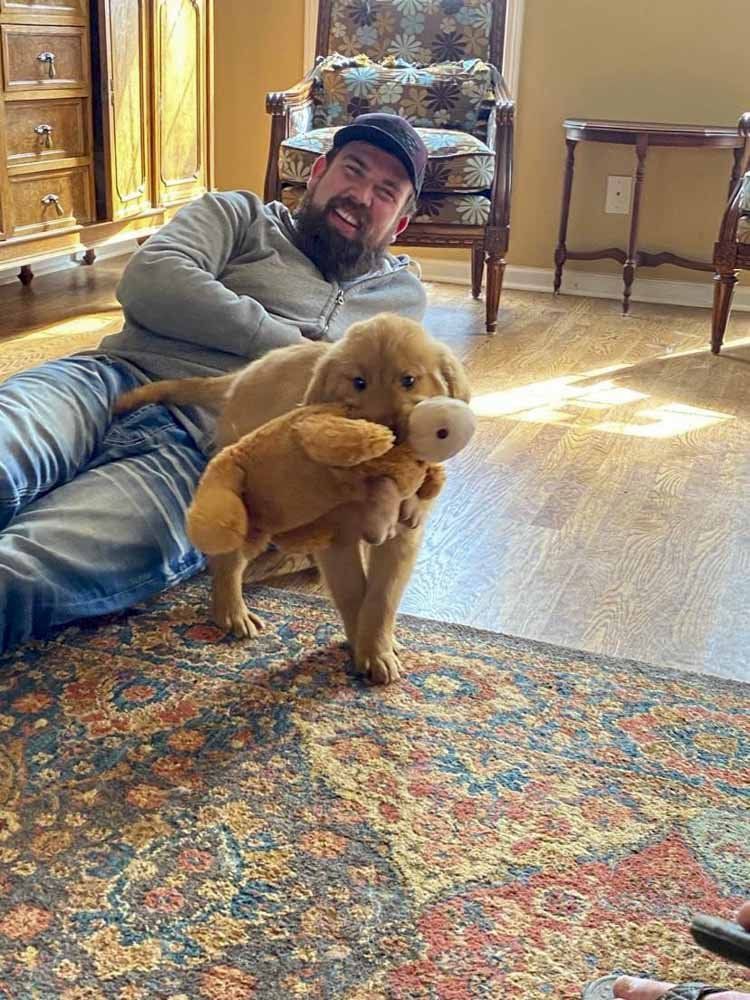 A man is laying on the floor holding a puppy.