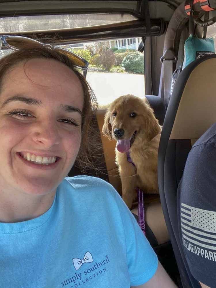 A woman is sitting in the back seat of a car with a puppy.