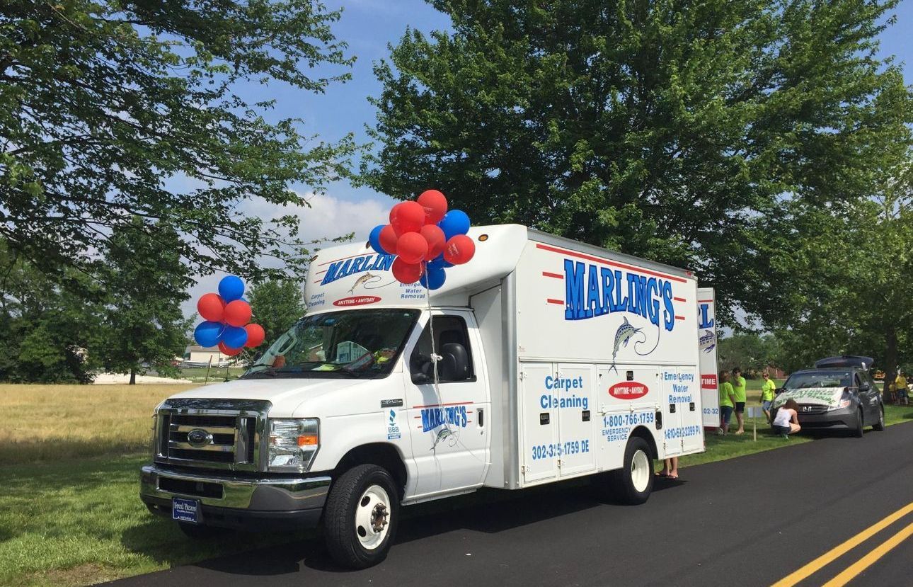 A white truck with red and blue balloons on top is parked on the side of the road.