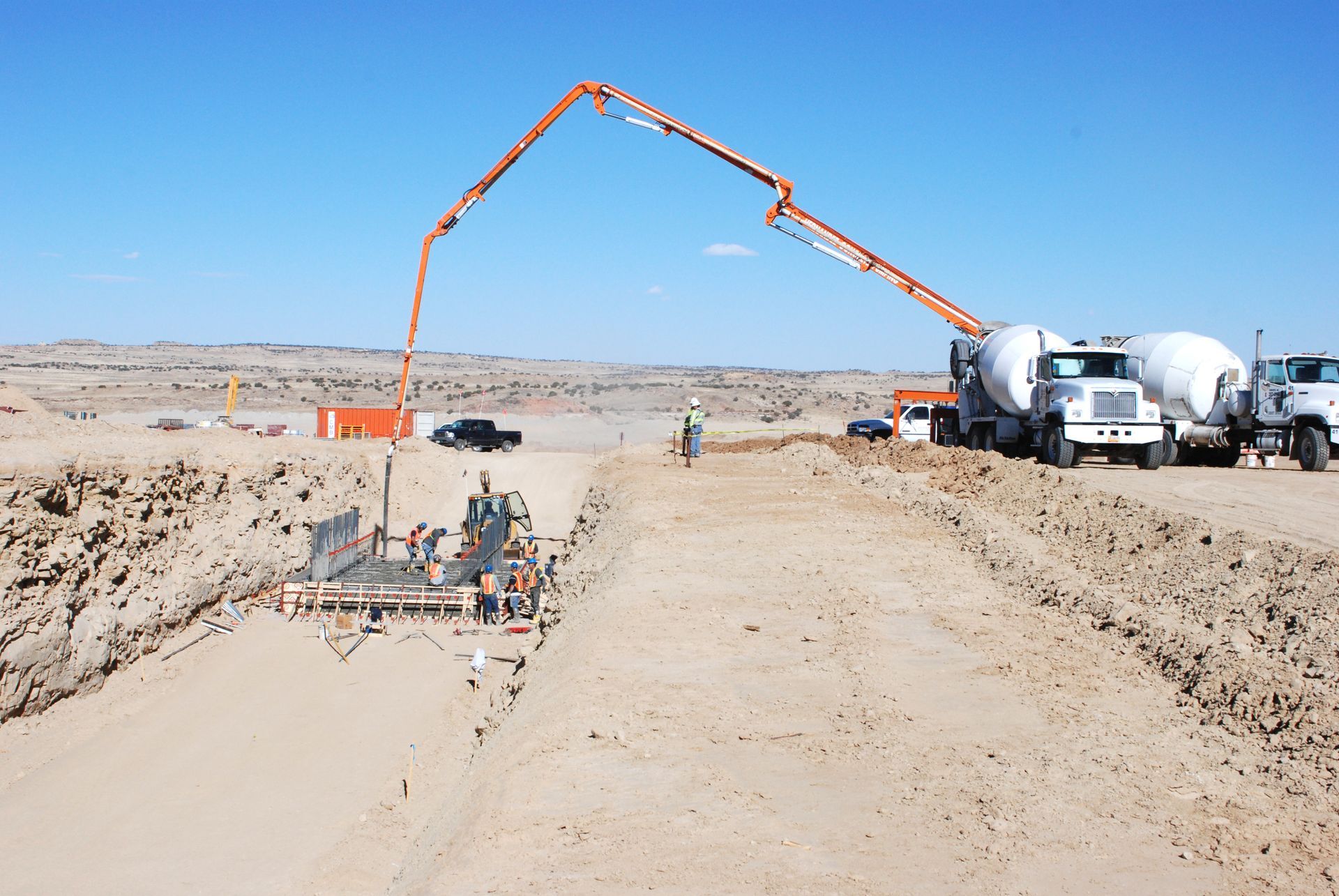 Concrete pump pouring at a road construction site with trucks and workers on a dusty desert road Concrete pump pouring at a road construction site with trucks and workers on a dusty desert road
