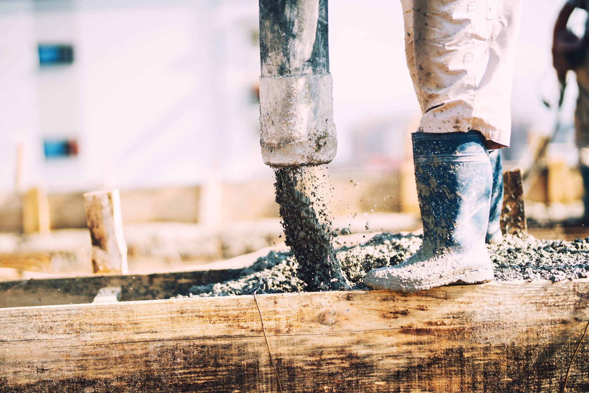 Concrete pumping services actively pouring cement into a wooden foundation structure at a job site.