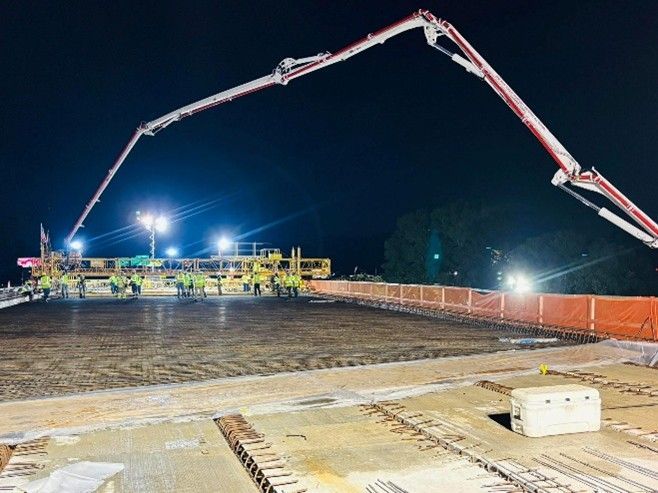 Concrete being poured on a bridge deck at night. Long pump arm extends over workers in bright safety vests. Concrete being poured on a bridge deck at night. Long pump arm extends over workers in bright safety vests.
