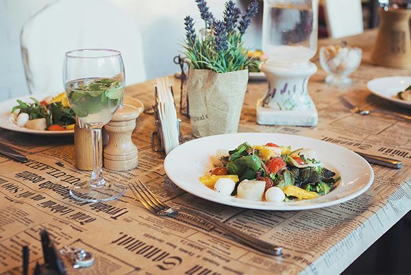 Table set for a meal: salad, water, wine glass, and lavender in a pot on a newspaper-covered tablecloth.
