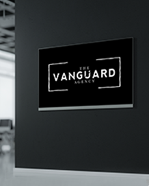 Black sign on black wall: “The Vanguard Agency” logo, white text within a white-lined rectangle.