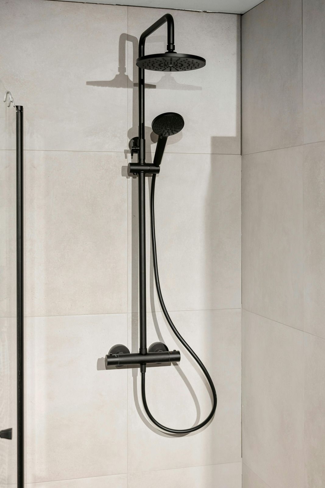Black shower fixture on light-colored tile wall with rain shower head and handheld shower.