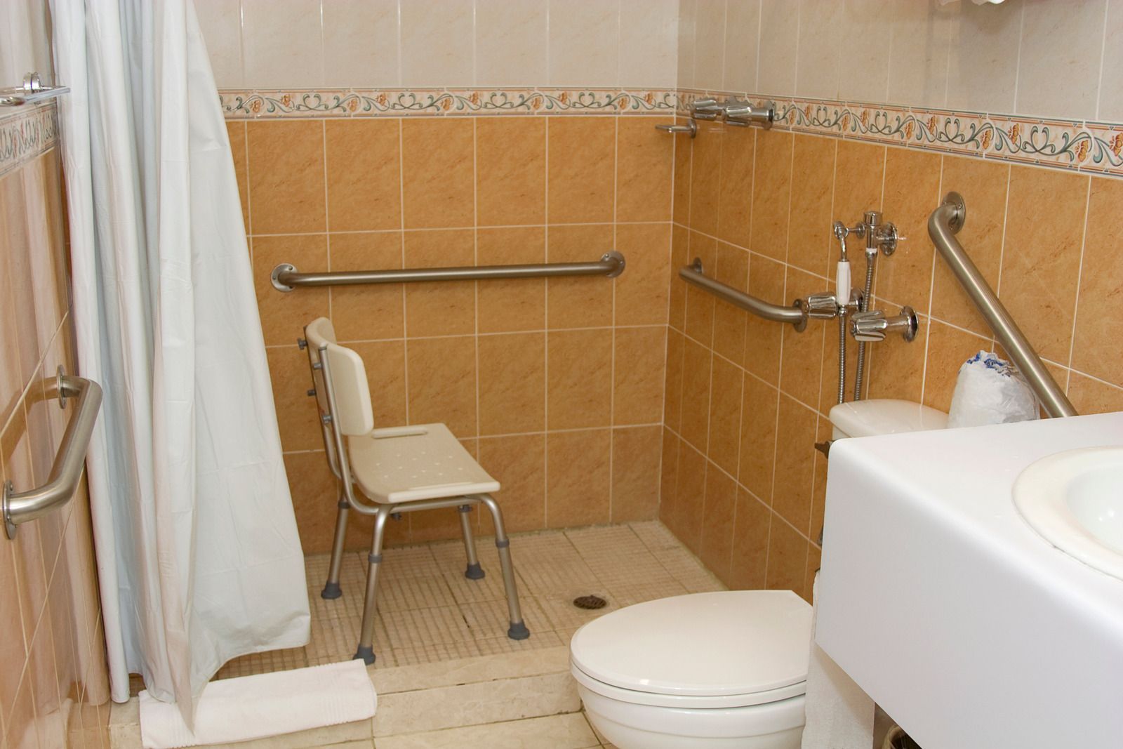 Accessible bathroom with a shower, toilet, sink, and safety bars.