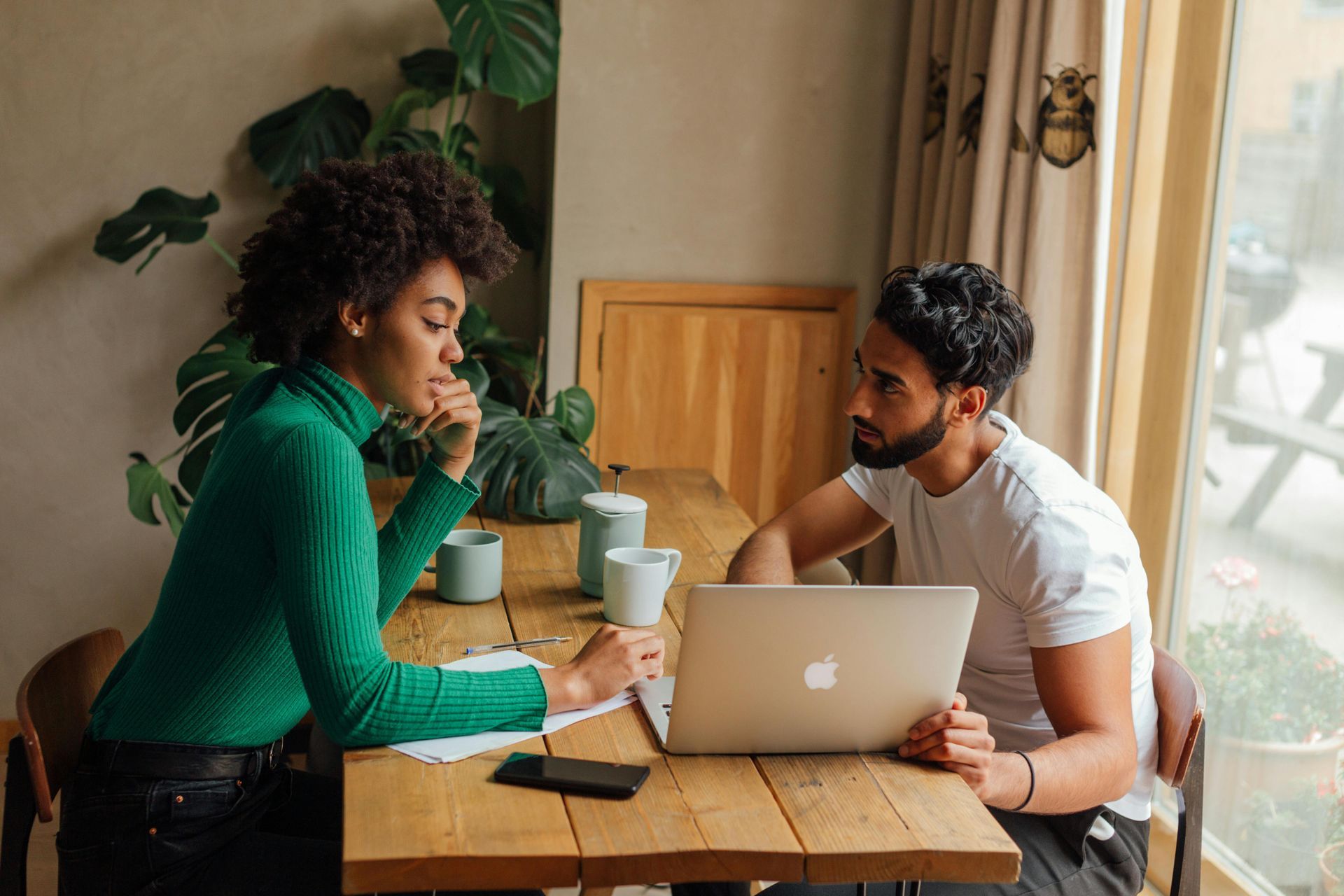 Couple sitting across from each other on a table while sharing a laptop.
