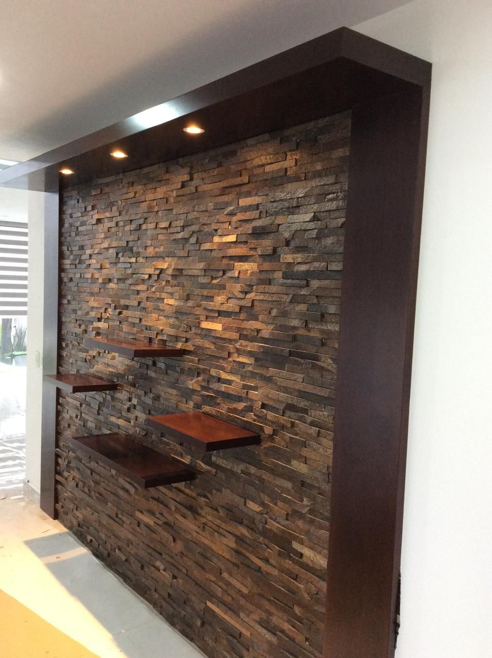 Pared con acento de piedra con estantes flotantes, molduras de madera oscura y luces empotradas.