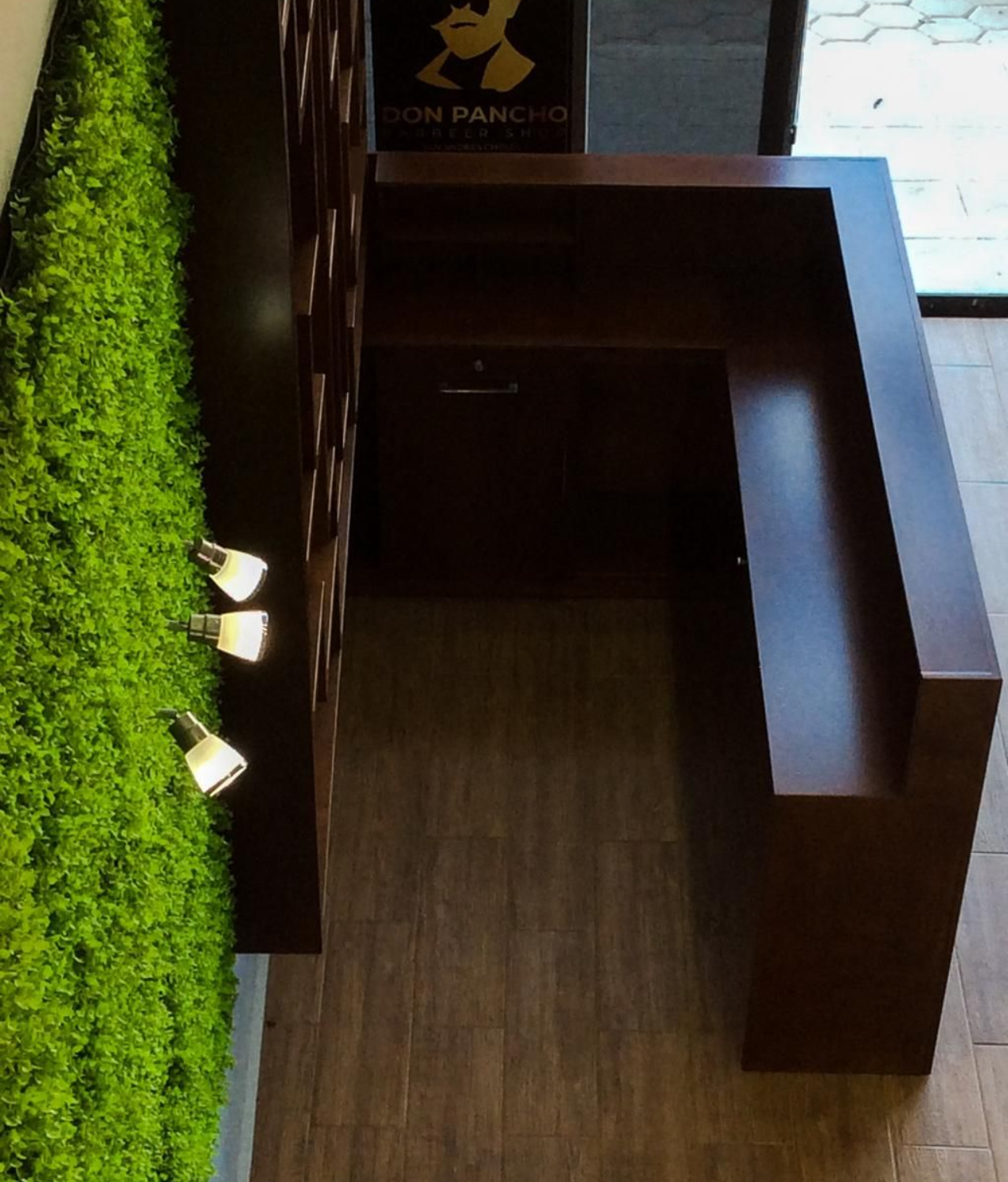 Mostrador y estantes de madera oscura con pared de musgo verde y luces.