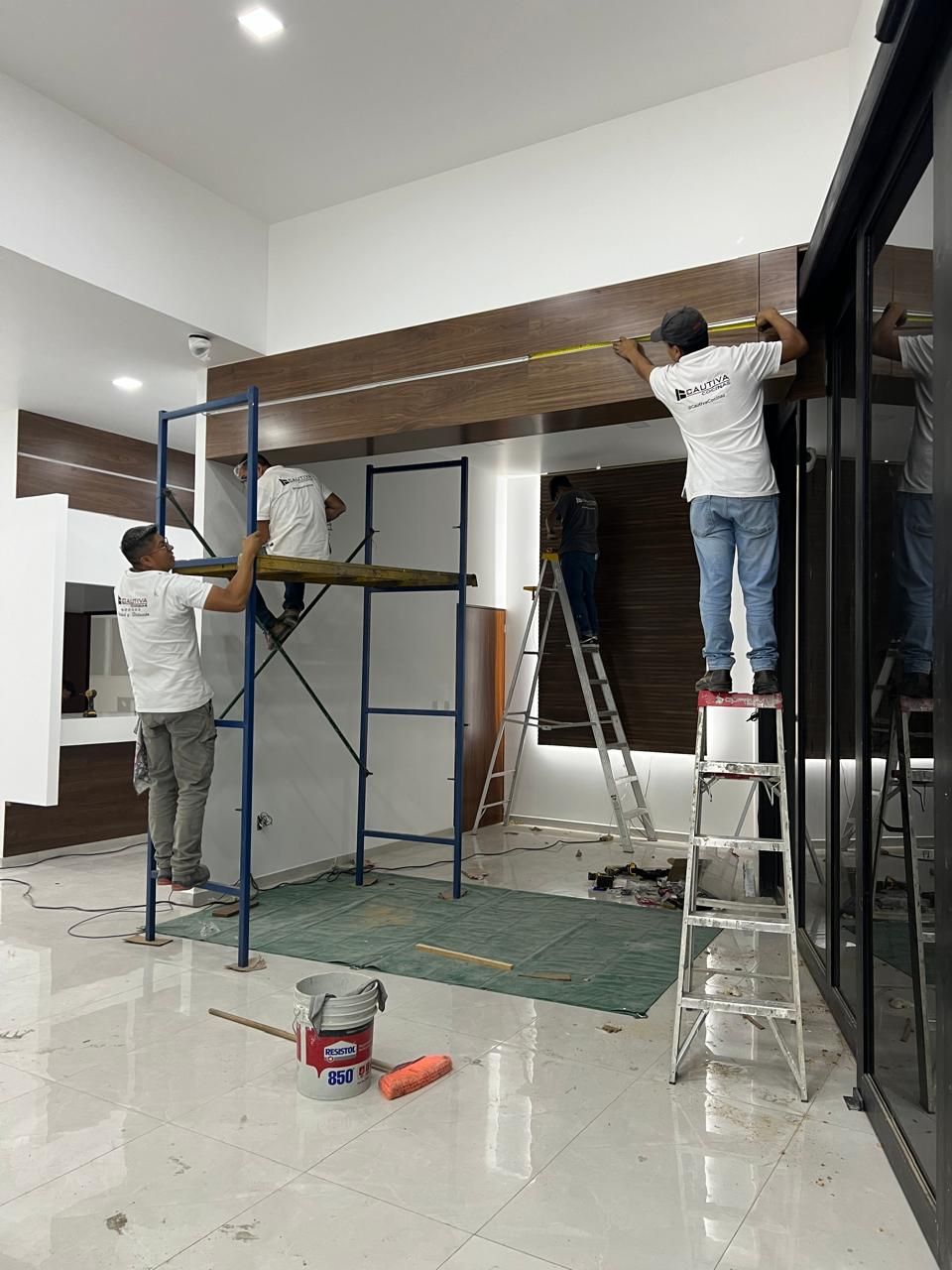 Trabajadores instalando paneles de madera en un mostrador de recepción en una habitación muy iluminada.