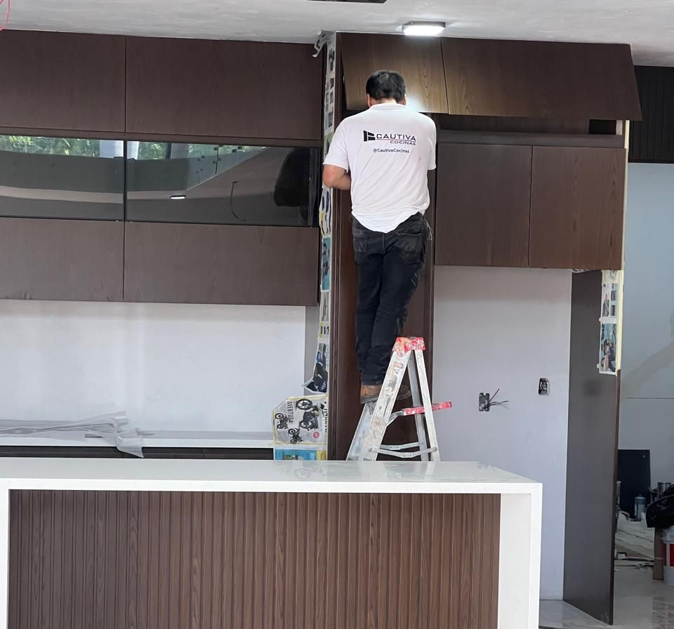 Persona en escalera instalando gabinetes de cocina, madera marrón oscuro.
