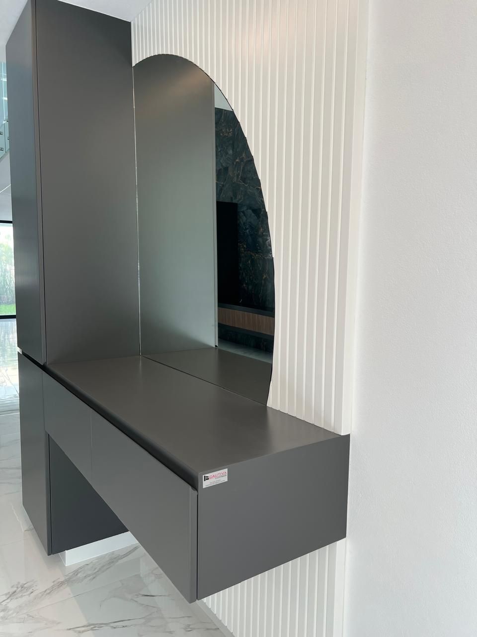 Tocador flotante gris con espejo y armario alto contra una pared blanca texturizada.