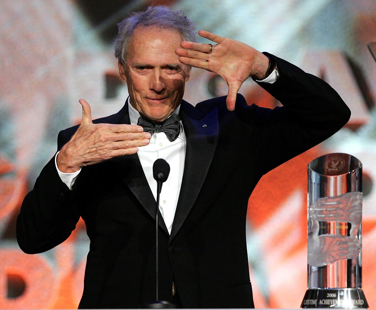 Clint Eastwood framing his face with his hands, at a podium, with an award next to him.