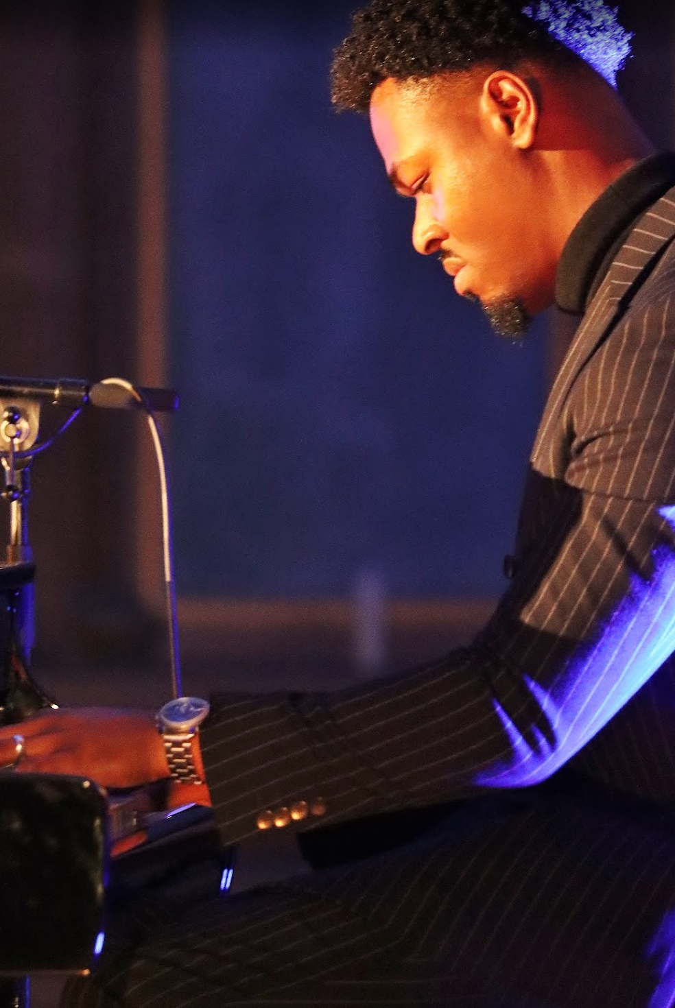 Man in vest and white shirt plays piano in a room.