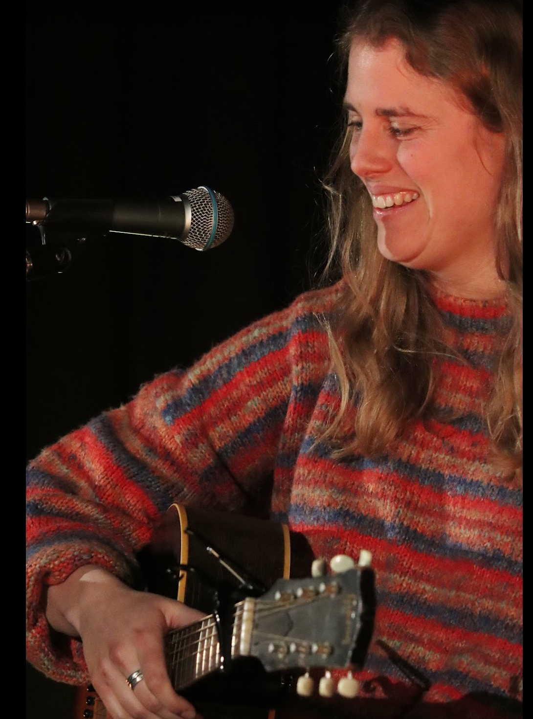 Woman singing and playing electric guitar on stage with purple lighting.