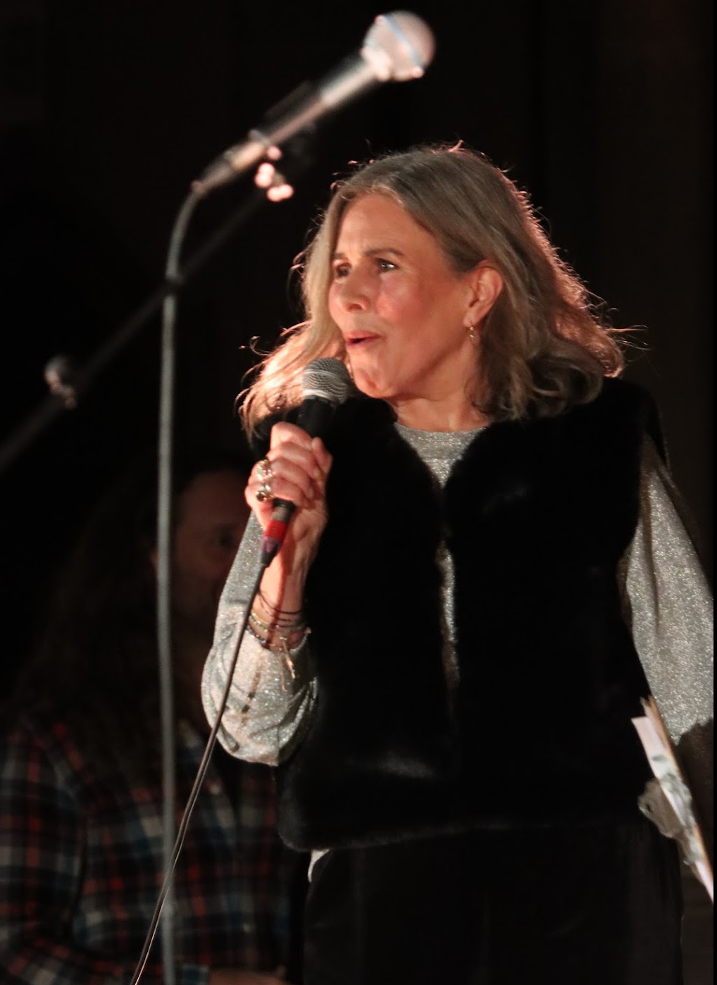 A person singing and playing piano on a stage, lit by a spotlight. Bare feet. White attire.
