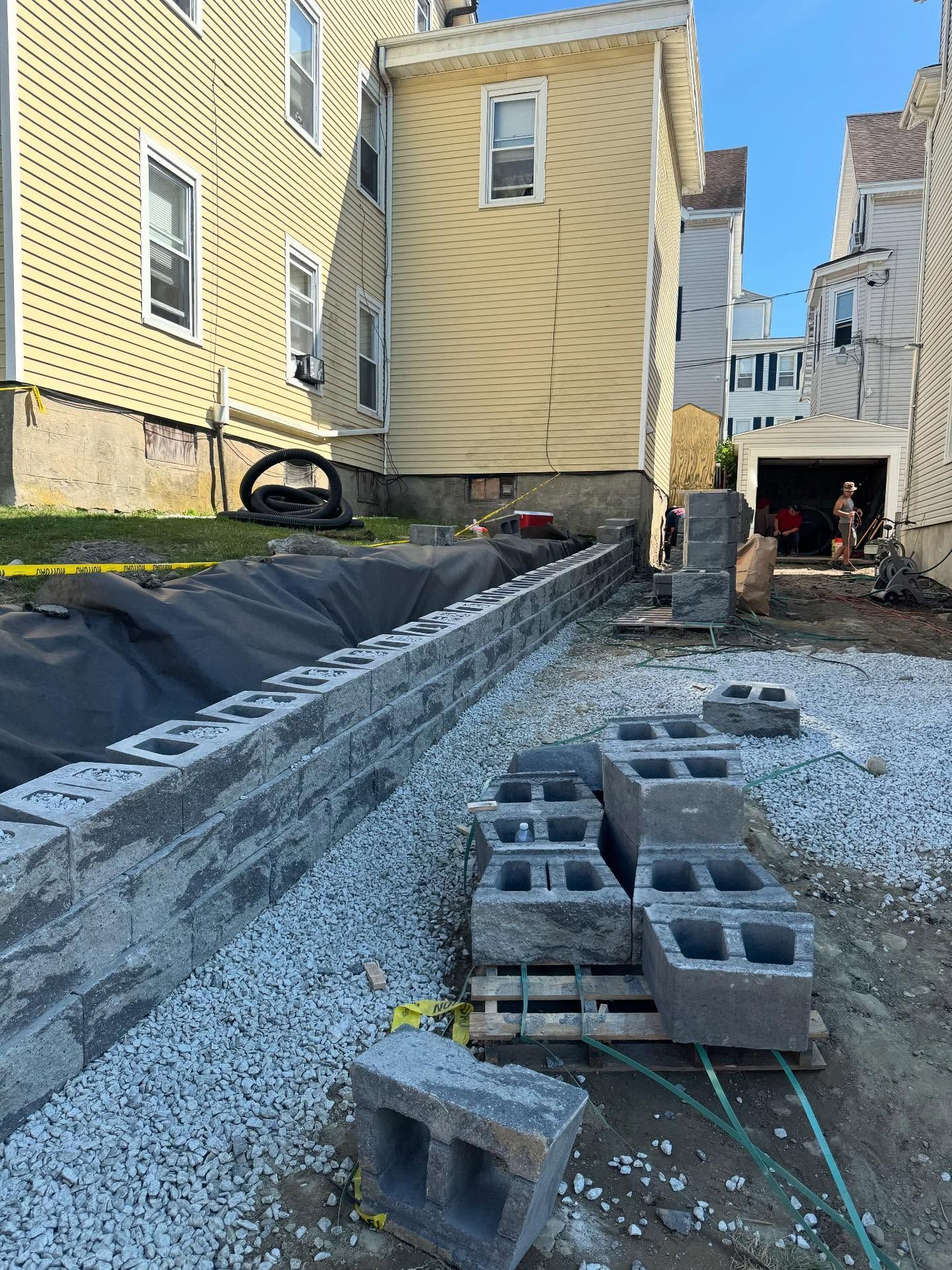 Construction site with gray retaining wall being built near yellow houses.