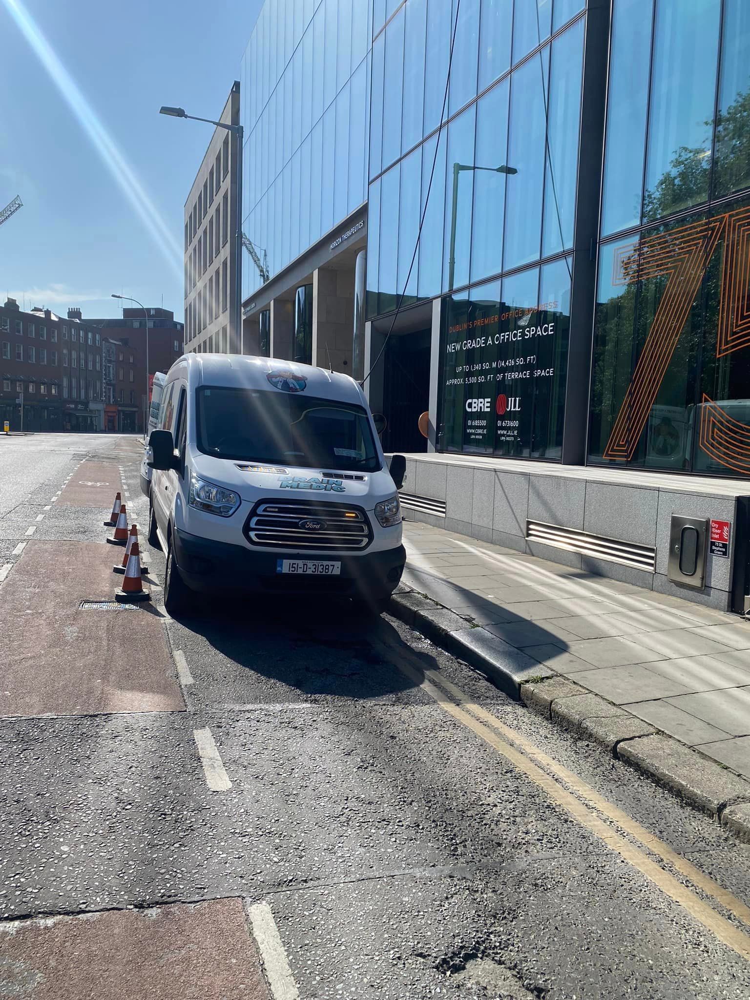 A white van is parked on the side of the road in front of a building.