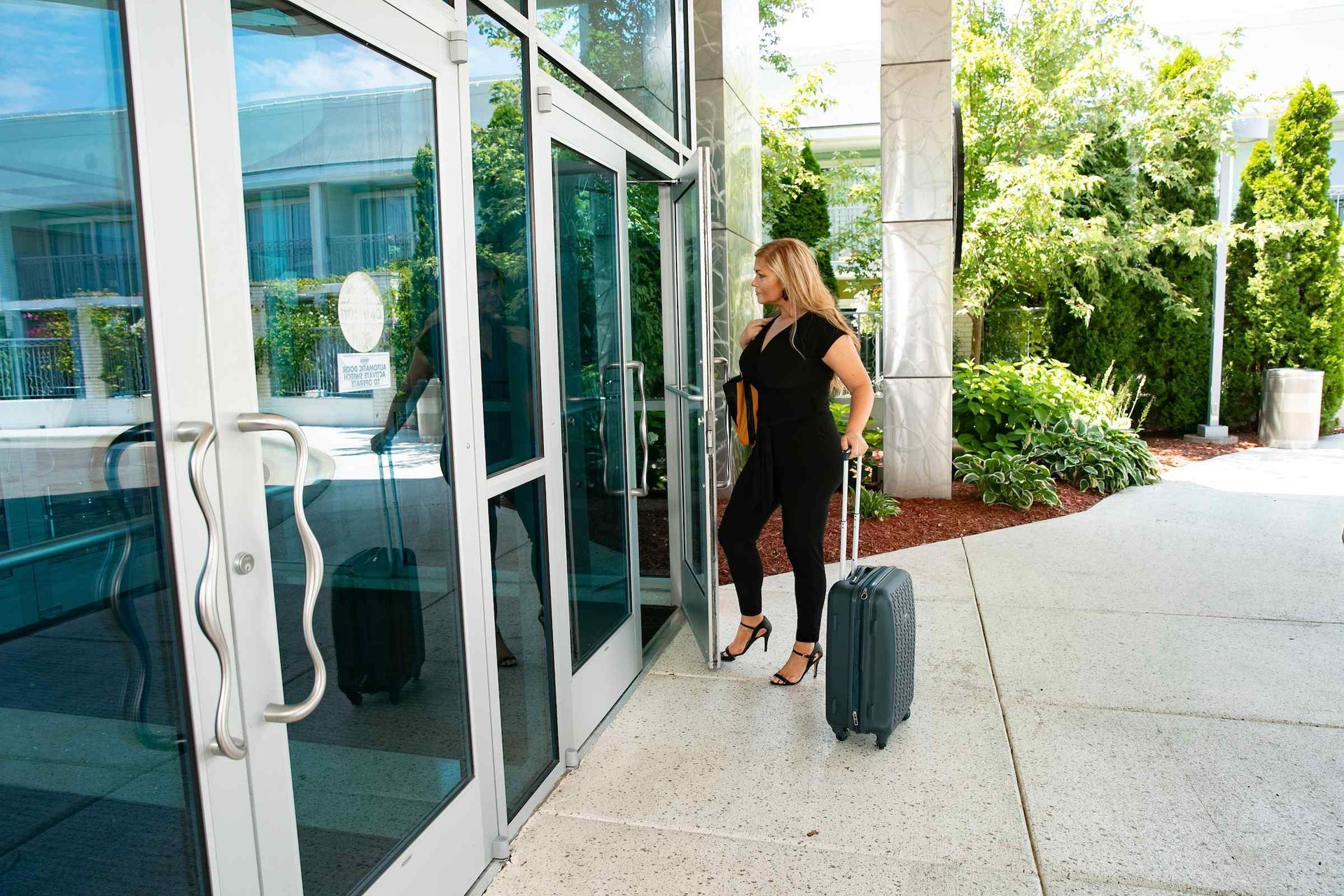 A woman is standing outside of a building with a suitcase.