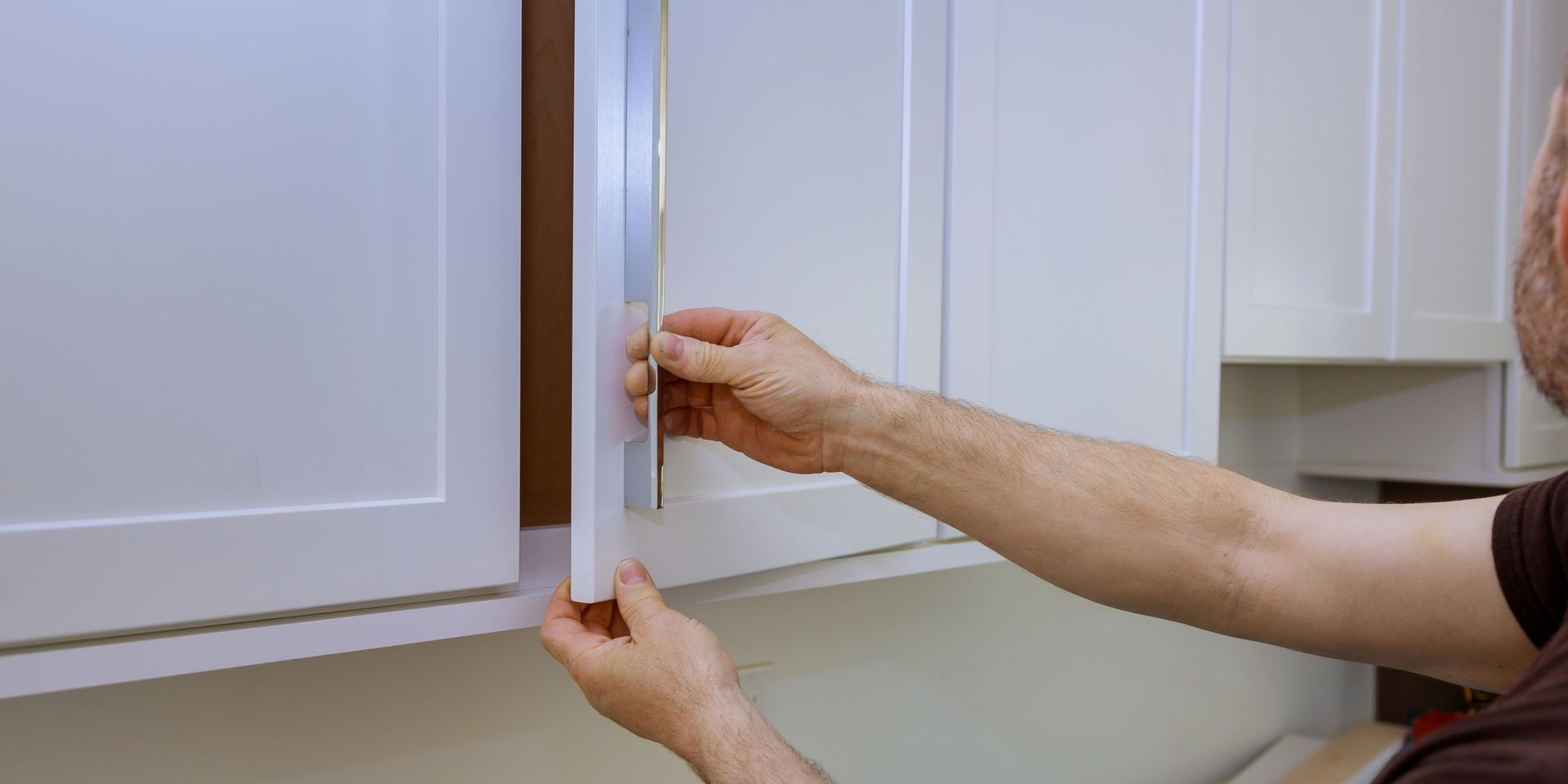 Person opening a white kitchen cabinet. They are using the handle.