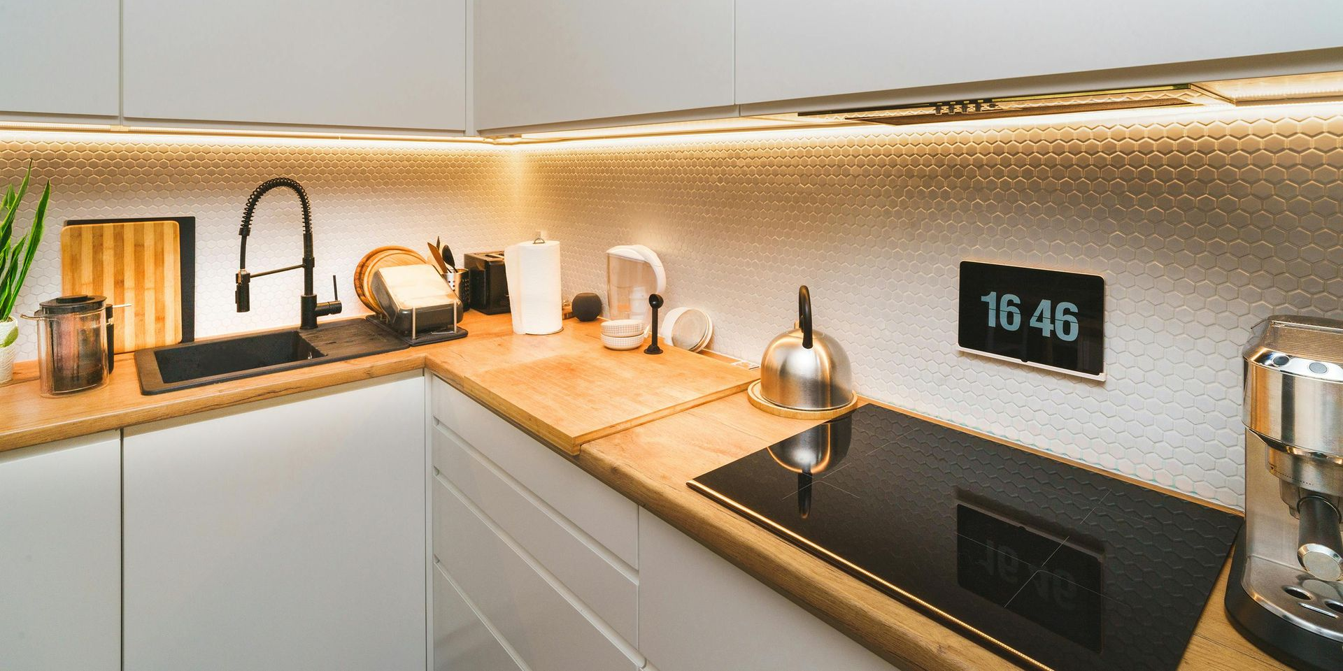 Modern kitchen with wooden countertops, black stovetop, and digital clock displaying 16:46.
