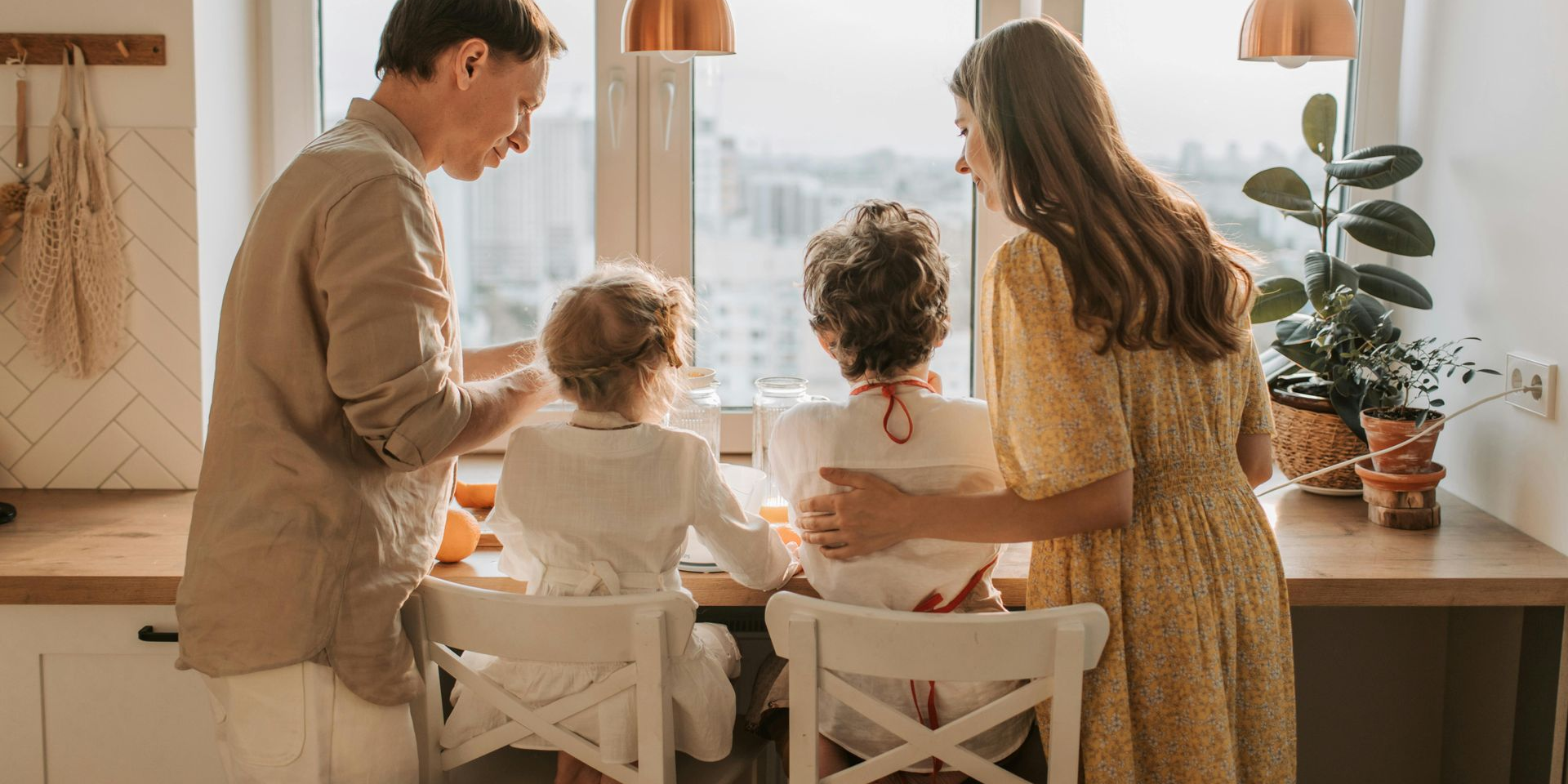 Family cooking in the kitchen: parents beside children, looking out the window, sunlight.