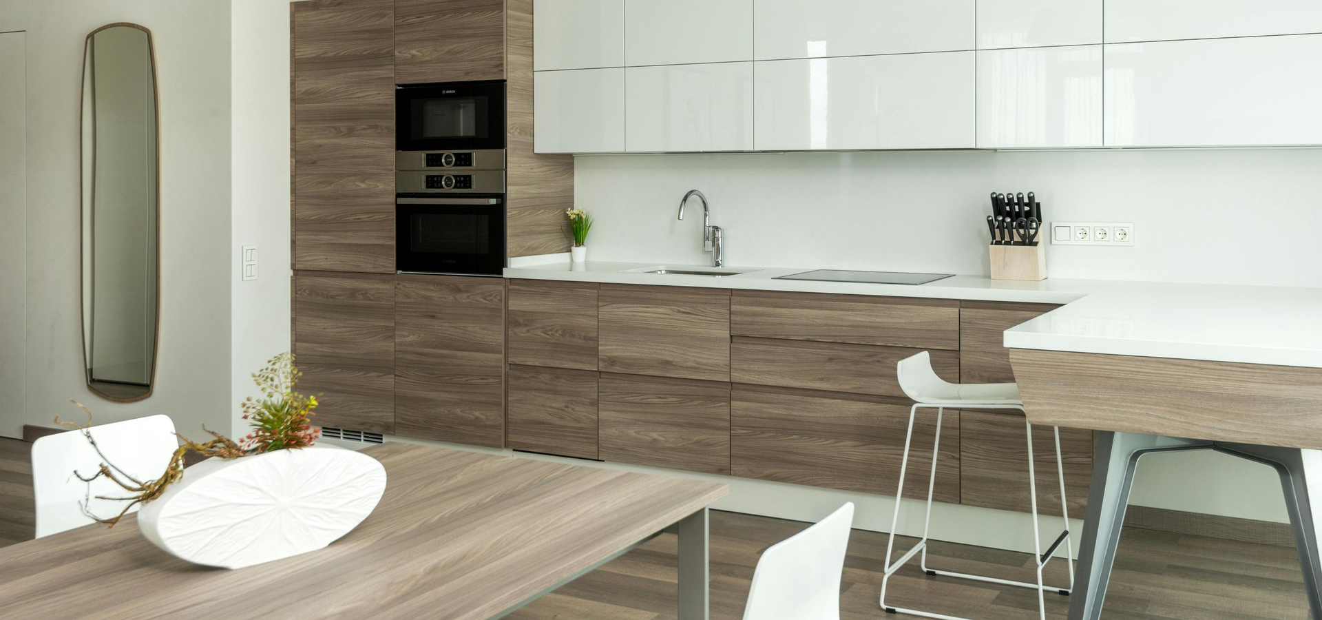 Modern kitchen with wood cabinetry, white countertops, and a dining table.