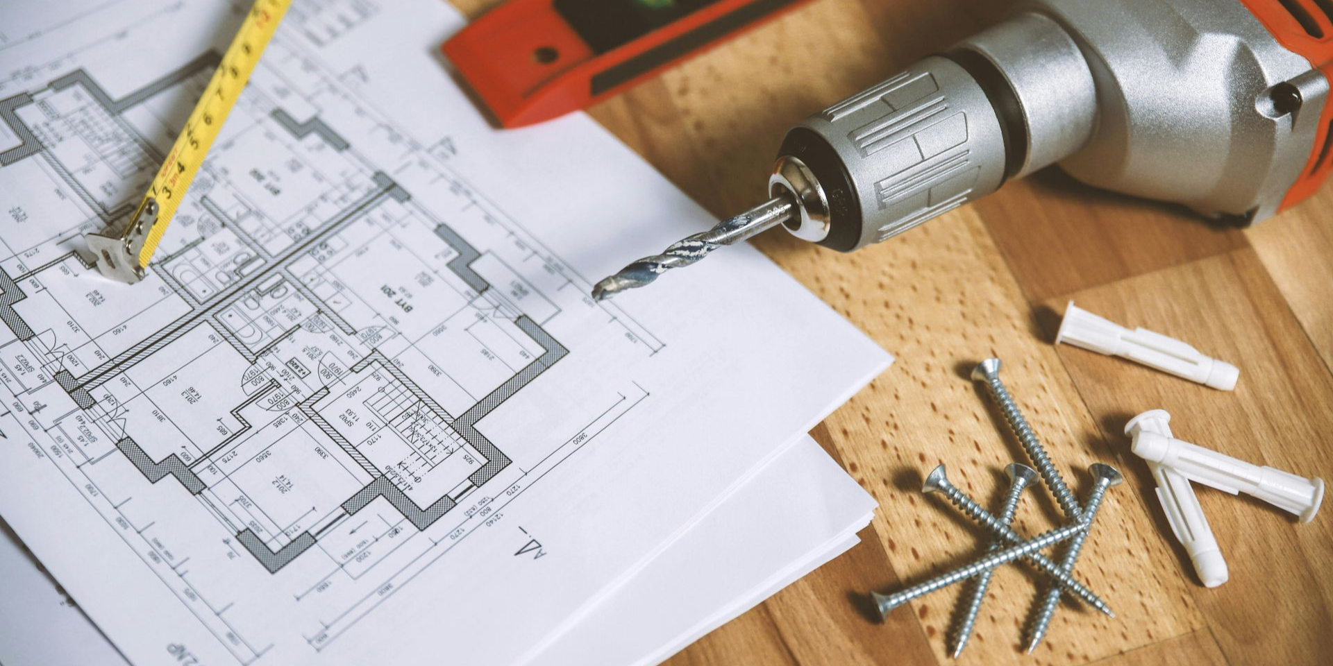 Construction tools on architectural plans, including a drill, tape measure, level, nails, and anchors.