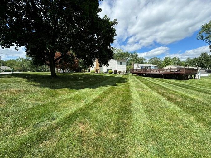 A lush green lawn with a deck in the background and a house in the background.