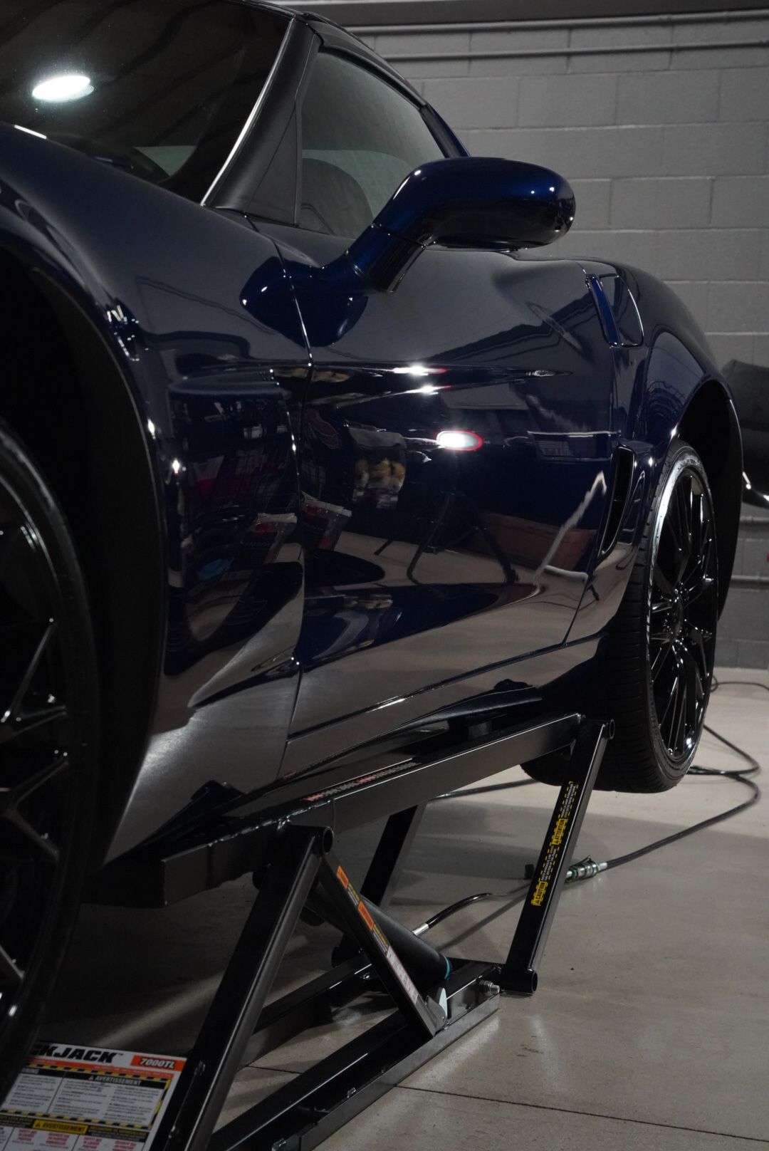 Dark blue sports car on a black car lift, showing reflections.