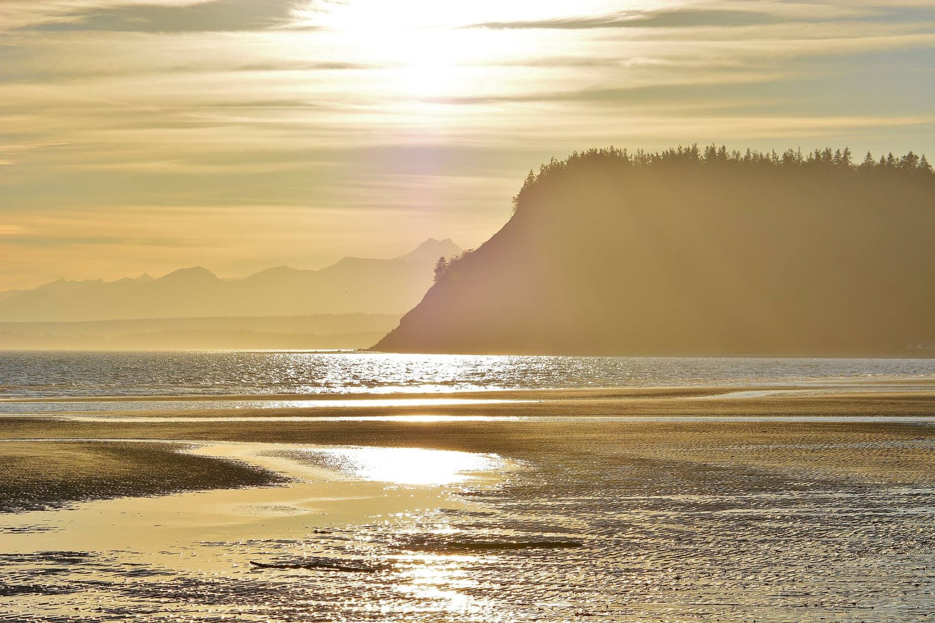 The sun is setting over a body of water with mountains in the background.