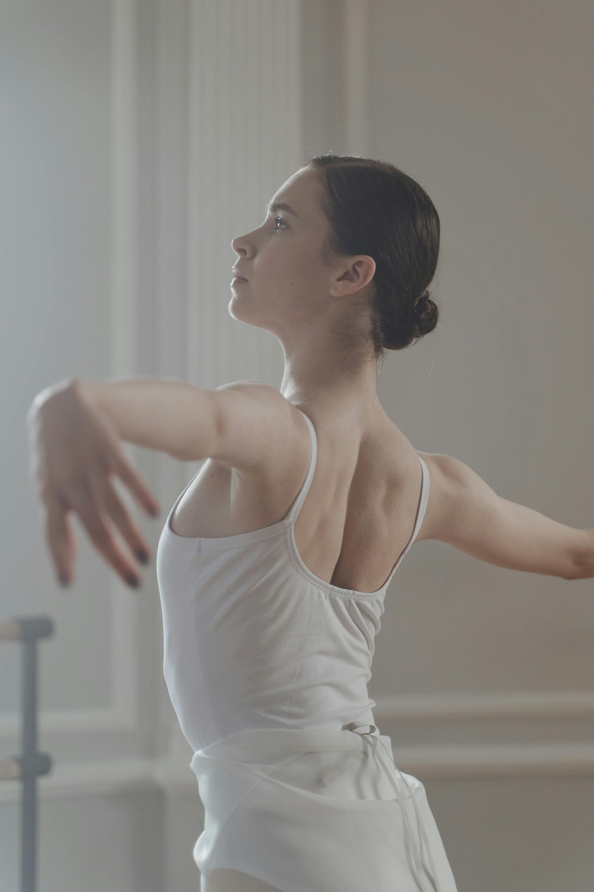 A young ballerina in a white dress is dancing in a dance studio.