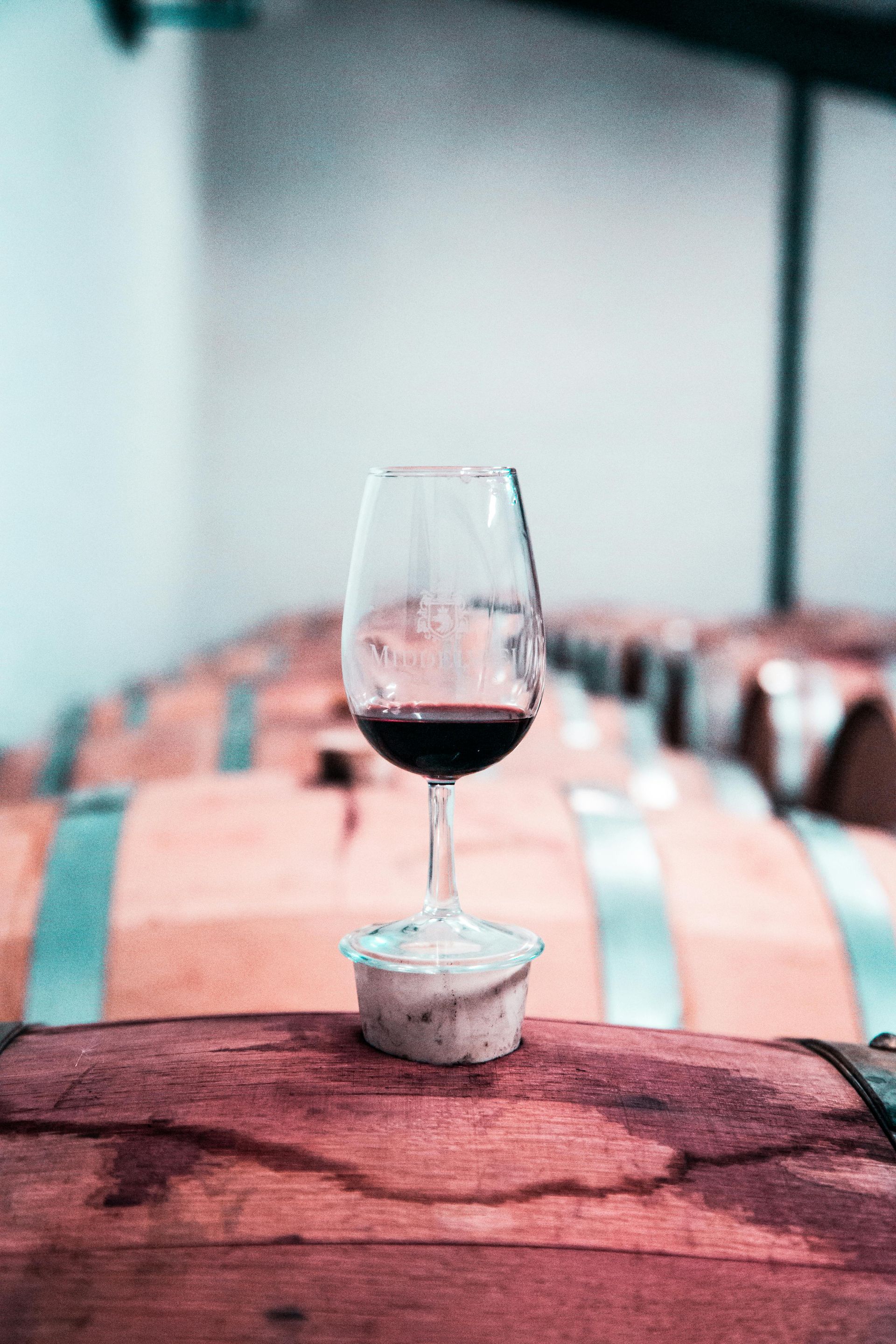A glass of red wine is sitting on top of a wooden barrel.