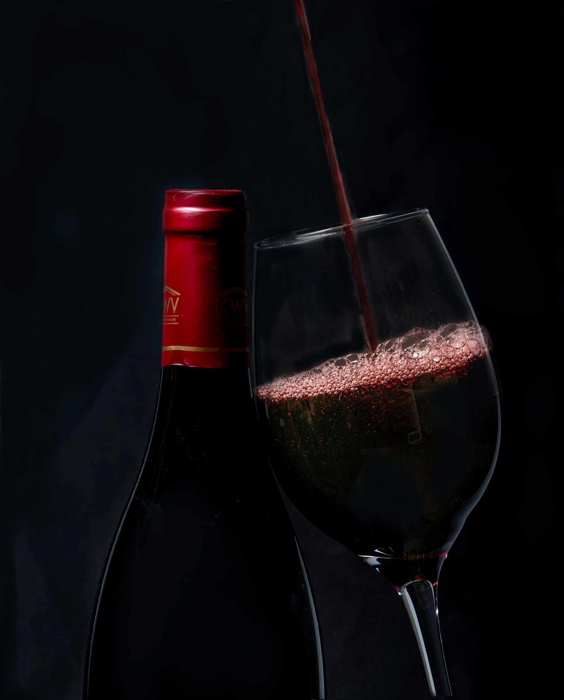 A bottle of wine is next to a glass of wine.