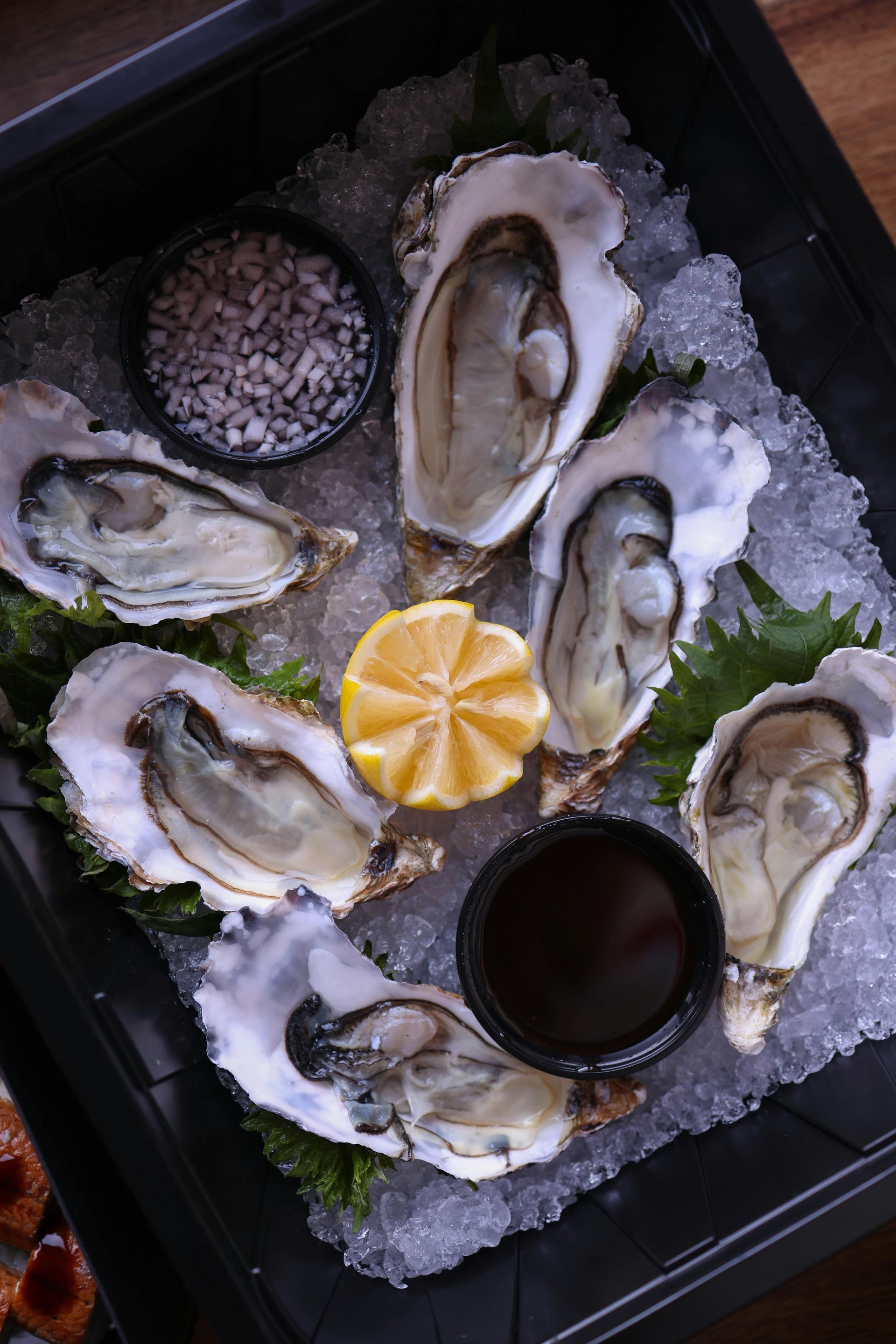 A tray of oysters on ice with a lemon slice and sauce.