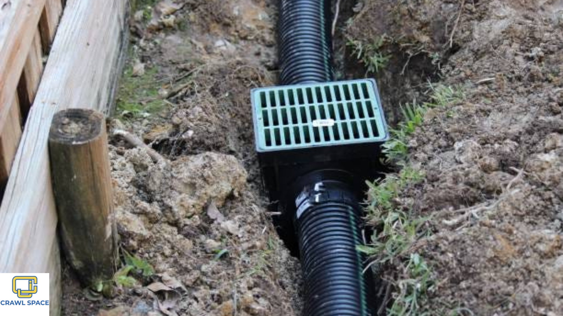 A black pipe is being installed in the ground next to a wooden fence.