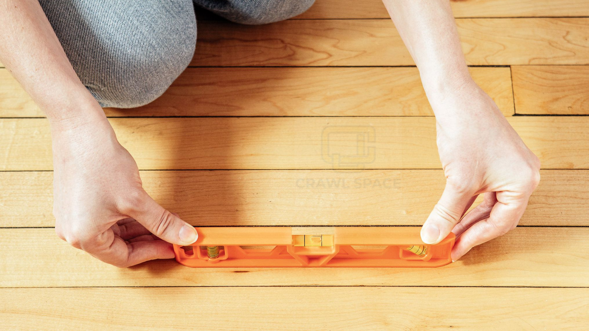 A person is using an orange level on a wooden floor.