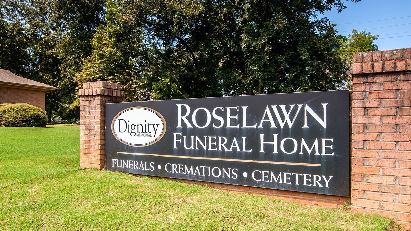 A sign for roselawn funeral home is on a brick wall.