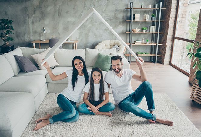 A family is sitting on the floor in a living room holding a piece of paper in the shape of a house.