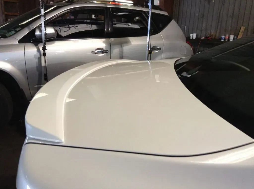 White car hood with a silver SUV in the background, likely in a garage.