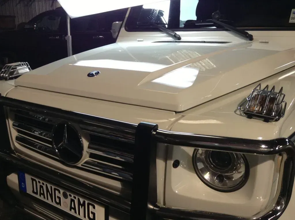 White Mercedes-Benz G-Wagon SUV with chrome grill and bumper guard, parked indoors.
